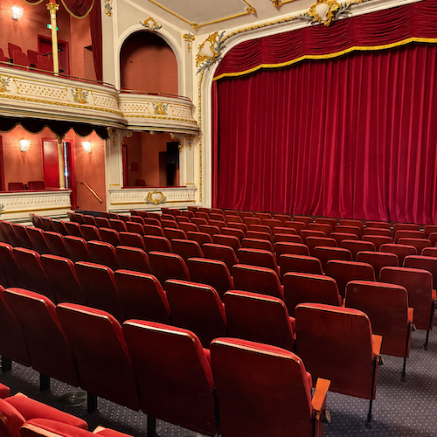 Leerer Theatersaal mit roten Sesseln und rotem Samtvorhang