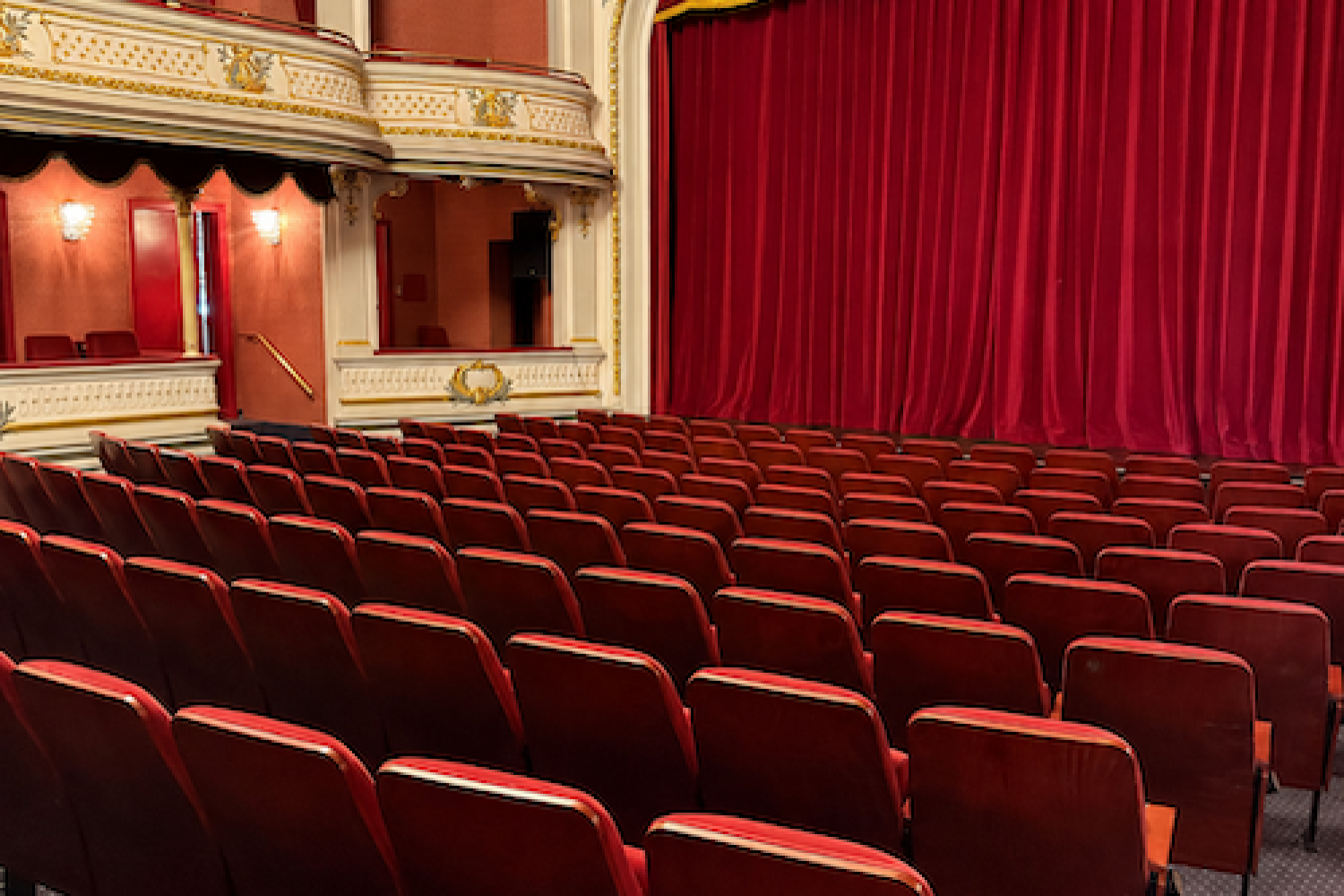 Leerer Theatersaal mit roten Sesseln und rotem Samtvorhang