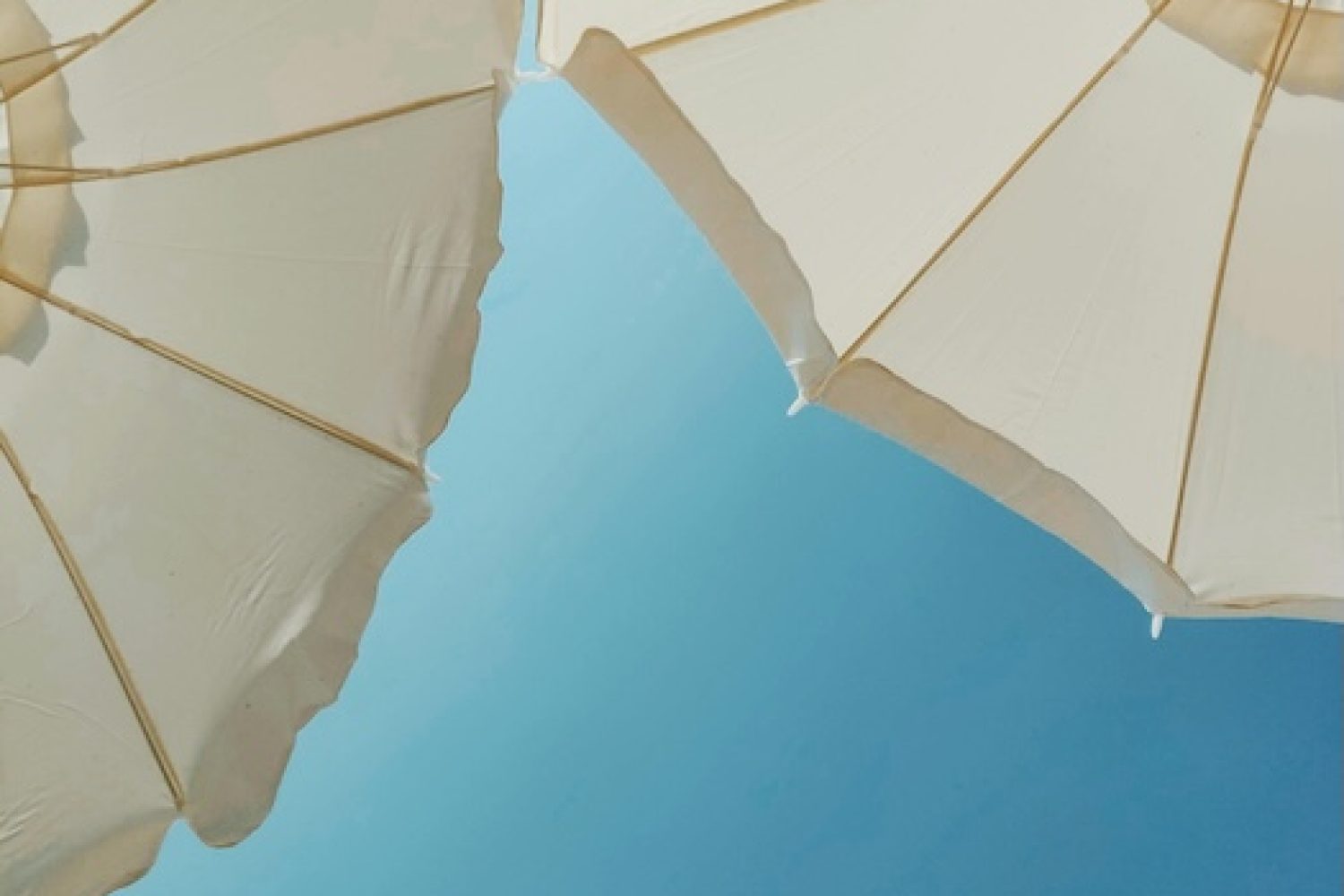 Zwei von unten fotografierte Sonnenschirme mit blauem Himmel als Hintergrund
