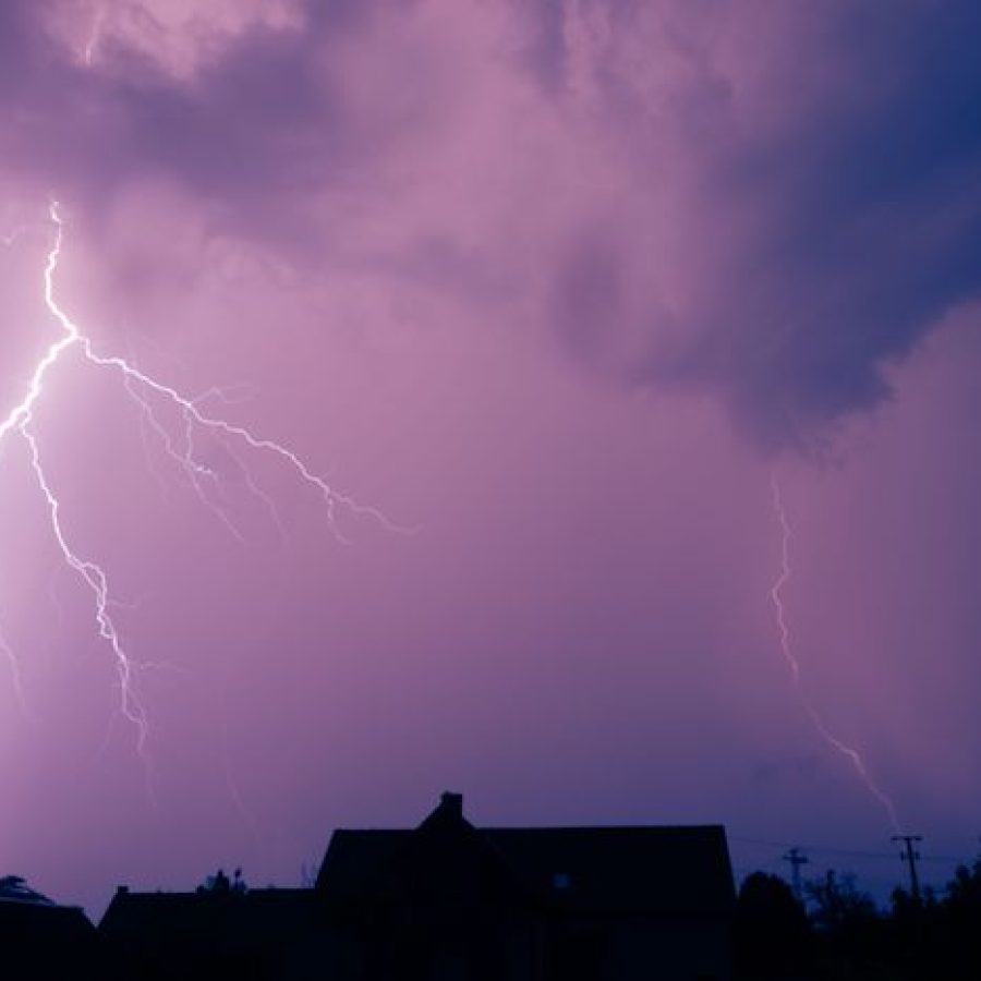 Symbolbild für Unwetter: ein Haus in einer Sturmnacht ist am Horizont zu sehen, obendrüber ist ein Blitz sichtbar.